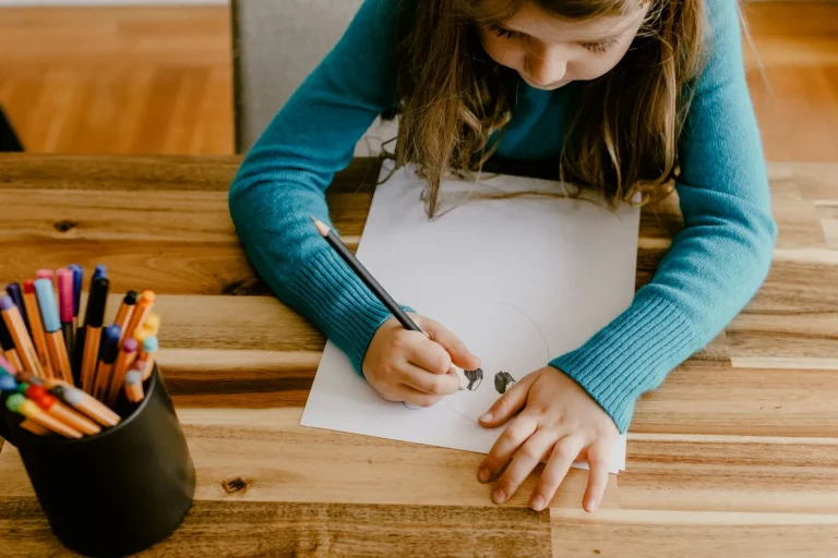 Petite fille assise à table avec des crayons de couleur devant une feuille